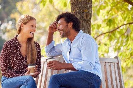 两个人在公园的长椅上笑着聊天，喝着咖啡